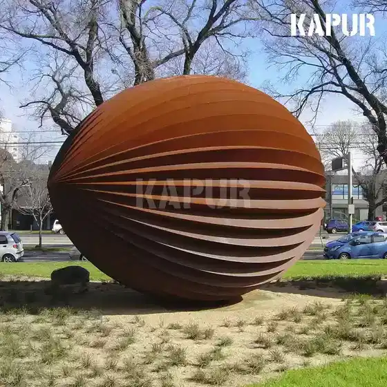Corten steel spherical outdoor garden sculpture standing in a natural garden setting with plants and soil around the base