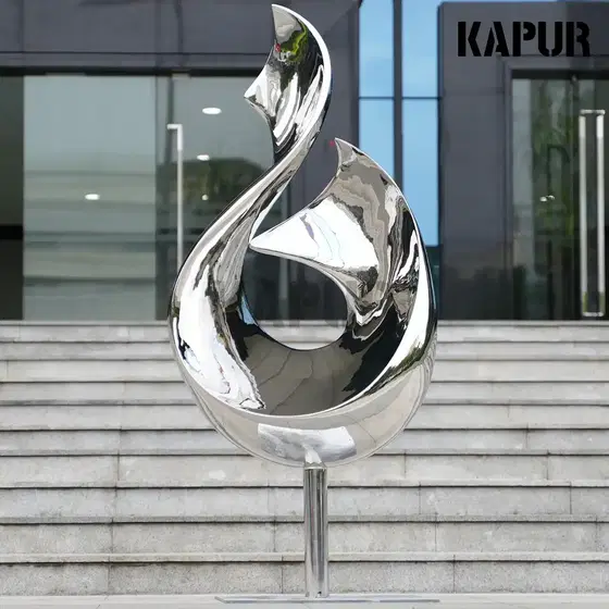 Polished stainless steel twisted ribbon sculpture standing on a paved outdoor plaza