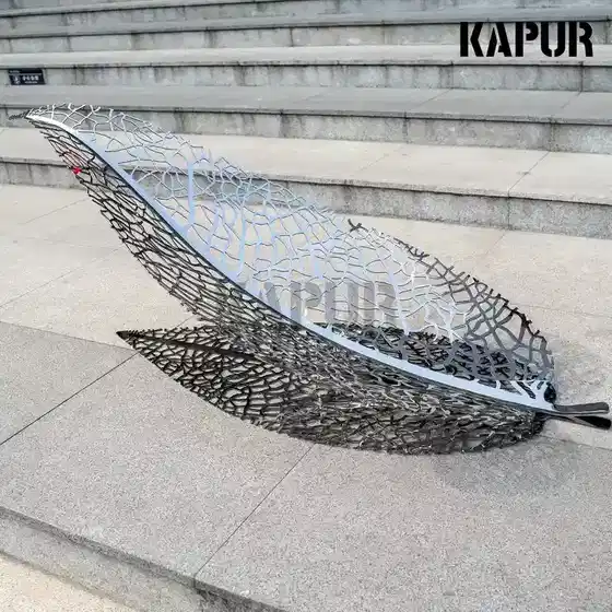 Polished stainless steel leaf sculpture standing in an outdoor garden setting with soft natural light