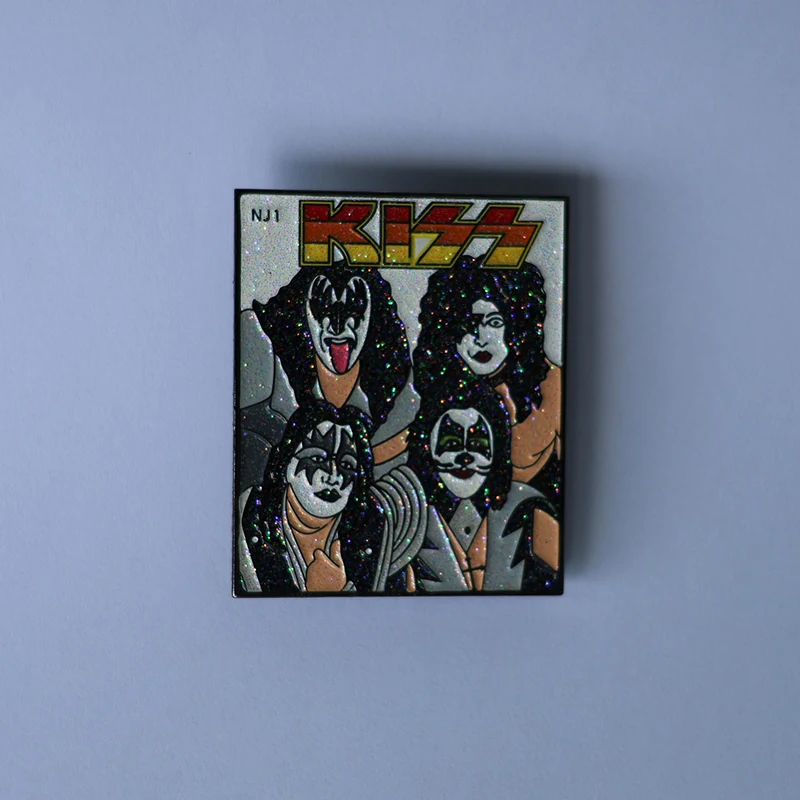 Retro glitter enamel lapel pin of the classic KISS band lineup with face paint and glitter details on a polished gold base