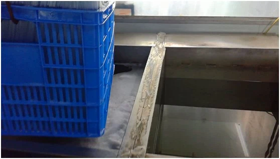 Blue plastic mesh crate resting on a stainless steel industrial machine