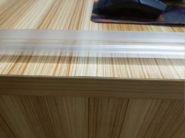 Translucent plastic extrusion profile lying on a wood-grain desk beside a mouse pad
