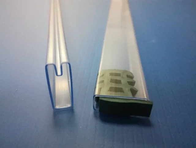 Two clear plastic extrusion profiles upright on a blue surface, one U-channel and one