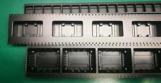 Black plastic injection-molded carrier trays with rectangular cavities and perforated edges arranged