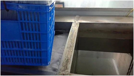 Blue plastic mesh crate resting on a stainless steel industrial machine
