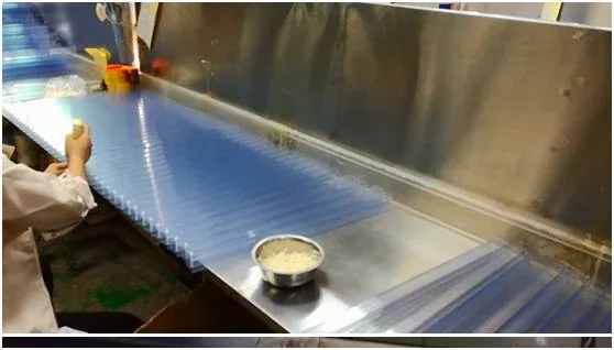 Worker at a stainless steel workbench handling a blue corrugated plastic sheet, with a metal bowl