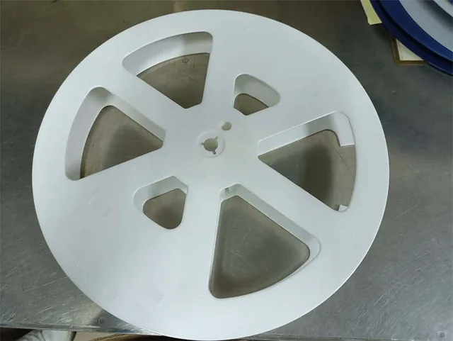 Large white machined plastic disc with wedge-shaped cutouts and a center hole