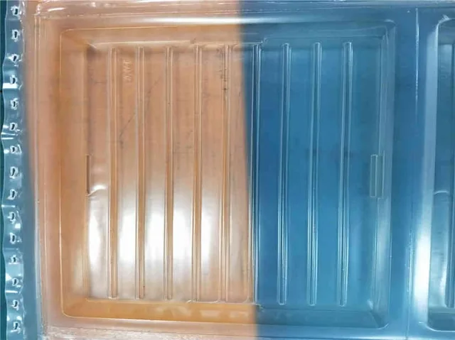Ribbed clear plastic thermoformed packaging tray with perforated edge, lit against split orange