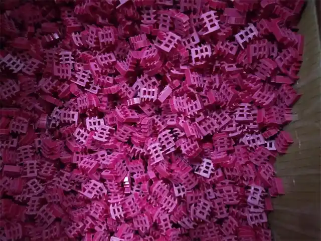 Bulk pile of small pink molded plastic grid-shaped parts filling