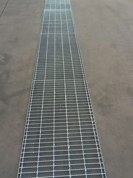 A long run of ditch steel grating covering a drainage channel across a concrete yard