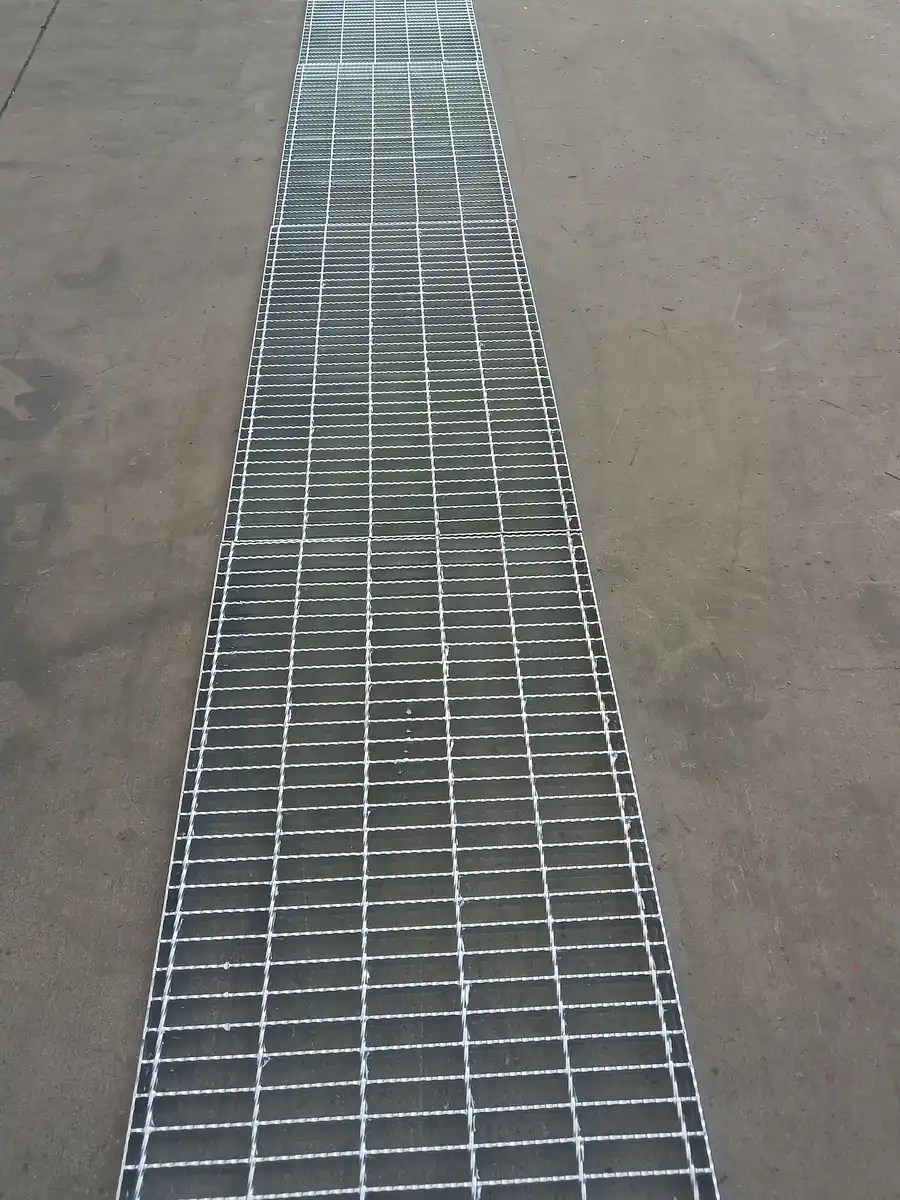 A long run of ditch steel grating covering a drainage channel across a concrete yard