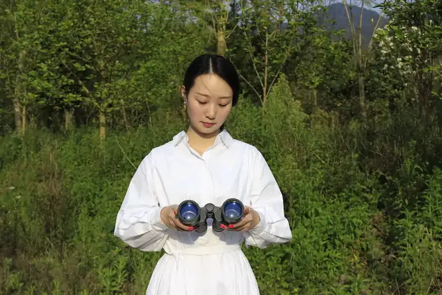 Woman in a white dress holding a blue handheld device outdoors in a grassy area