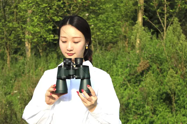 Woman holding black binoculars outdoors against a green forest background