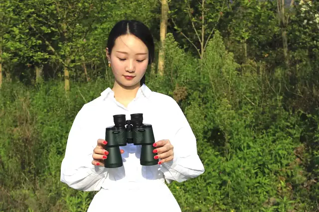 Woman holding a pair of black binoculars outdoors in front of trees