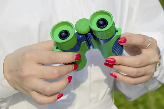 A person holding green and blue toy binoculars