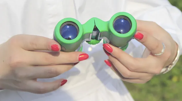 Hands holding green binoculars in front of a person wearing a white shirt