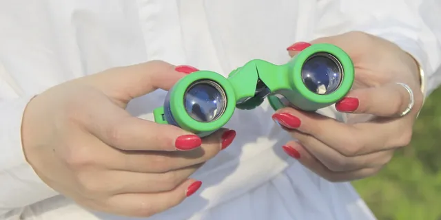 A pair of hands holding small green binoculars