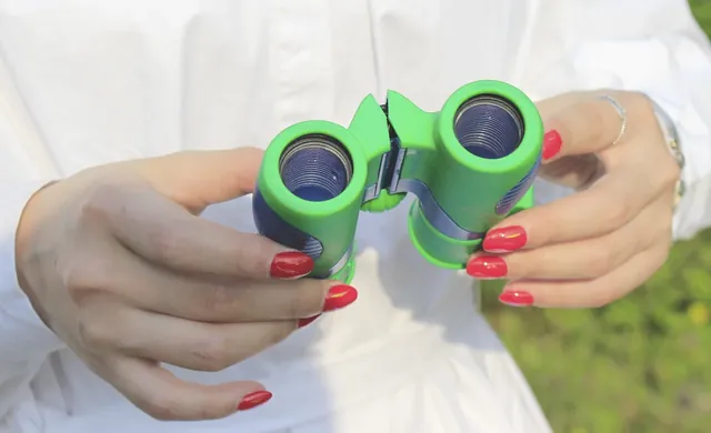 A person holding a pair of green and blue binoculars