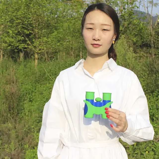 Woman in white shirt holding green and blue toy binoculars outdoors