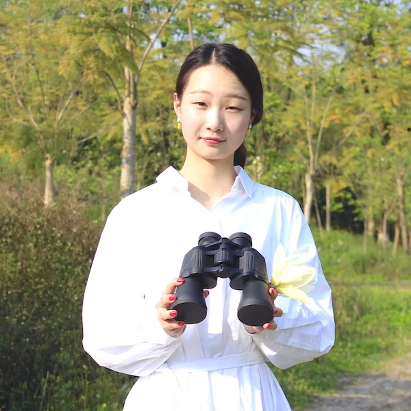 Woman in white shirt holding a pair of black binoculars outdoors