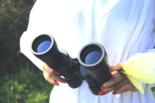 Hands holding black binoculars and a yellow flower, outdoors