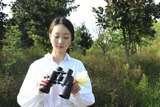 A woman wearing a white shirt holding black binoculars outdoors