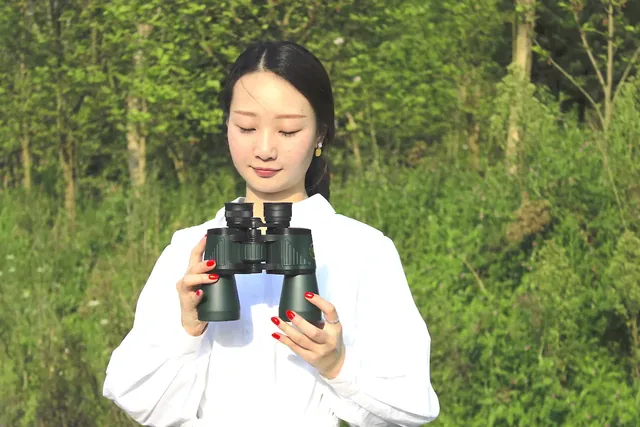 Woman in white shirt holding black binoculars outdoors with a green forest background