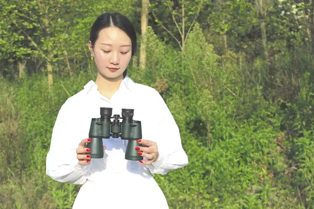 Woman in a white shirt holding a pair of black binoculars outdoors
