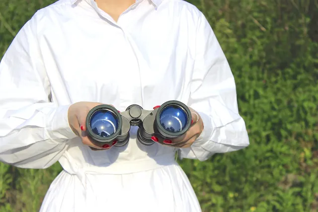 Person in a white shirt holding binoculars against a green background