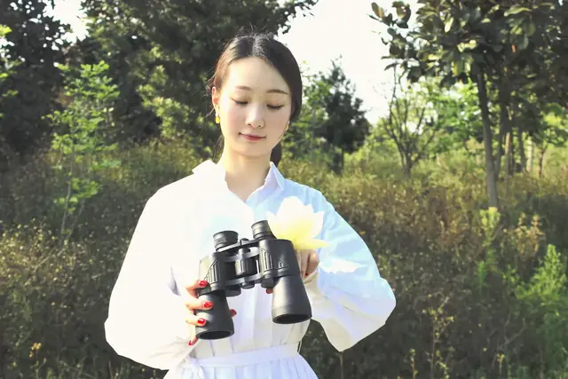 Woman in a white shirt holding black binoculars outdoors