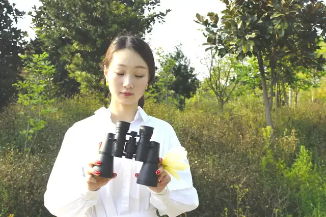 Woman holding a pair of black binoculars in an outdoor setting with trees