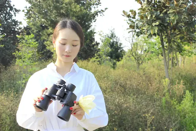 Woman in white shirt outdoors holding black binoculars and a cleaning cloth