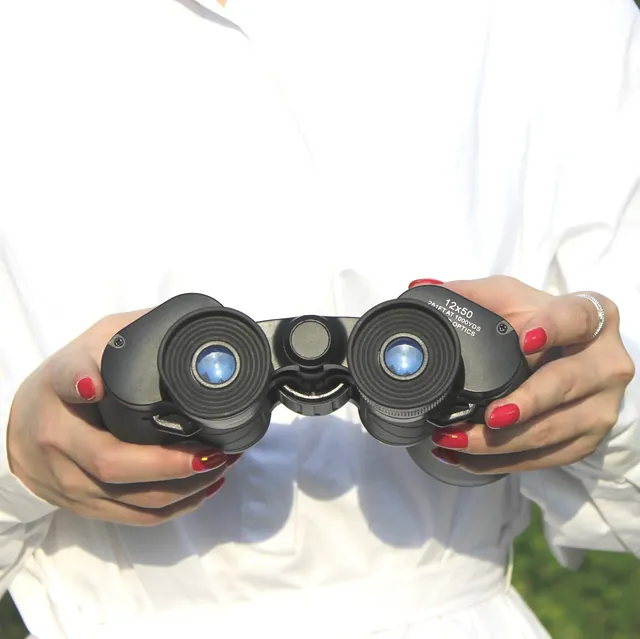 A person wearing a white shirt holds a pair of black binoculars towards the camera
