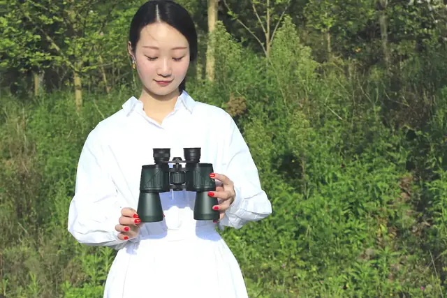 Woman in white shirt holding green binoculars in front of trees