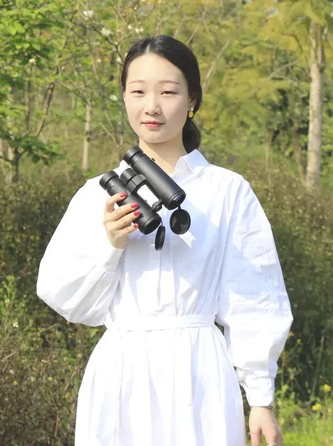 Woman in white shirt holding black binoculars outdoors