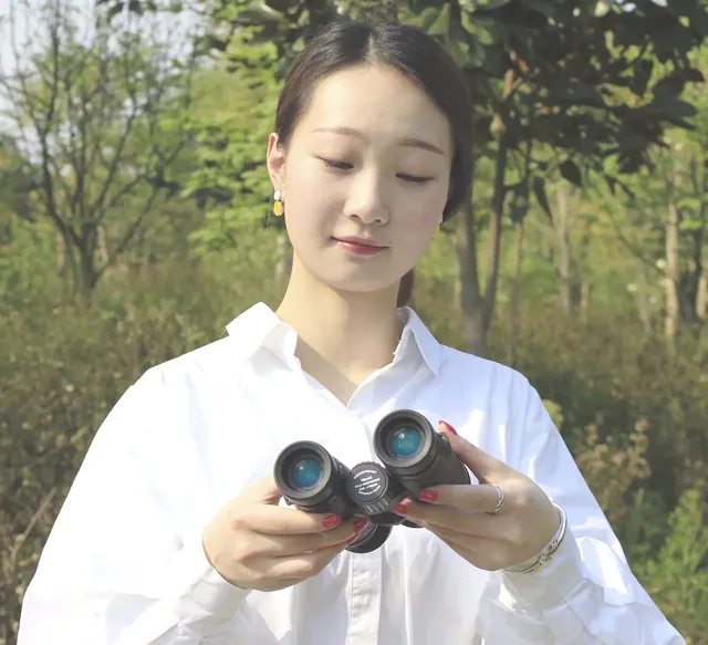 Woman in a white shirt holding a pair of black binoculars outdoors