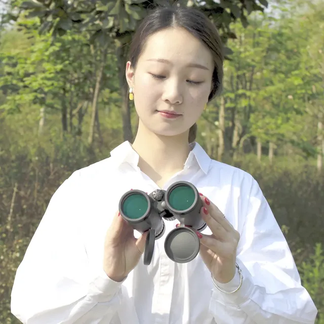 Woman holding a pair of binoculars with lens caps attached outdoors
