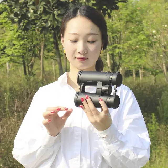 A woman in a white shirt holds a pair of black binoculars outdoors