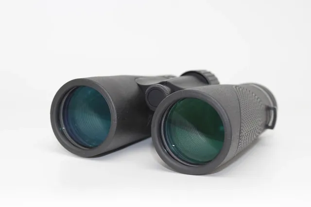 Close-up of the objective lenses of black binoculars on a white background