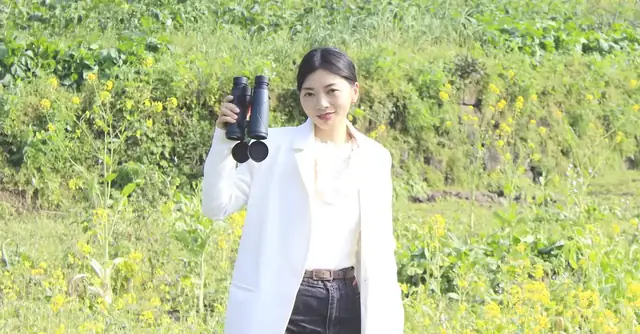 Woman in a white blazer holding binoculars in a field of yellow flowers