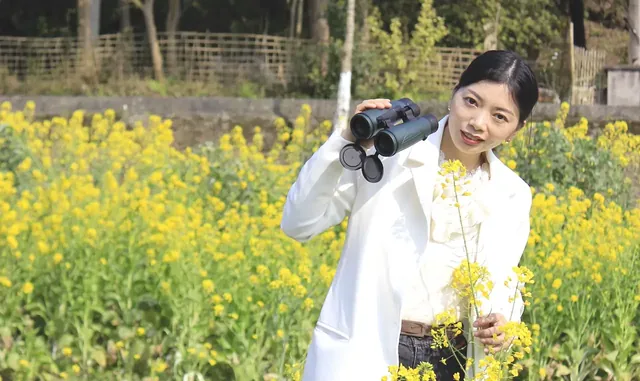 Woman in a white coat holding binoculars while standing in a field of yellow flowers