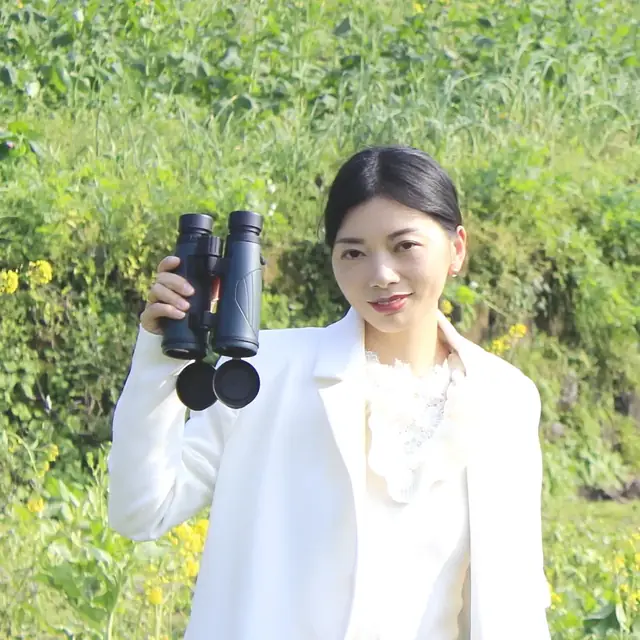 Woman in white blazer outdoors holding a pair of black binoculars with attached lens caps