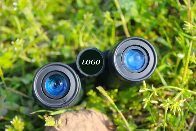 Top view of binoculars with blue lenses resting on grass with a placeholder logo overlay