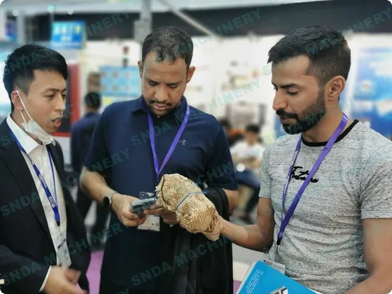 Three men wearing lanyards examine a wrapped sample together at a