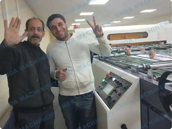 Two men waving and posing beside industrial machinery with a control panel in a factory