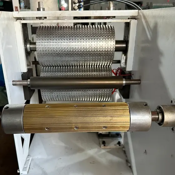 Industrial roller machine with perforated metal roller and brass ridged roller assembly in a workshop