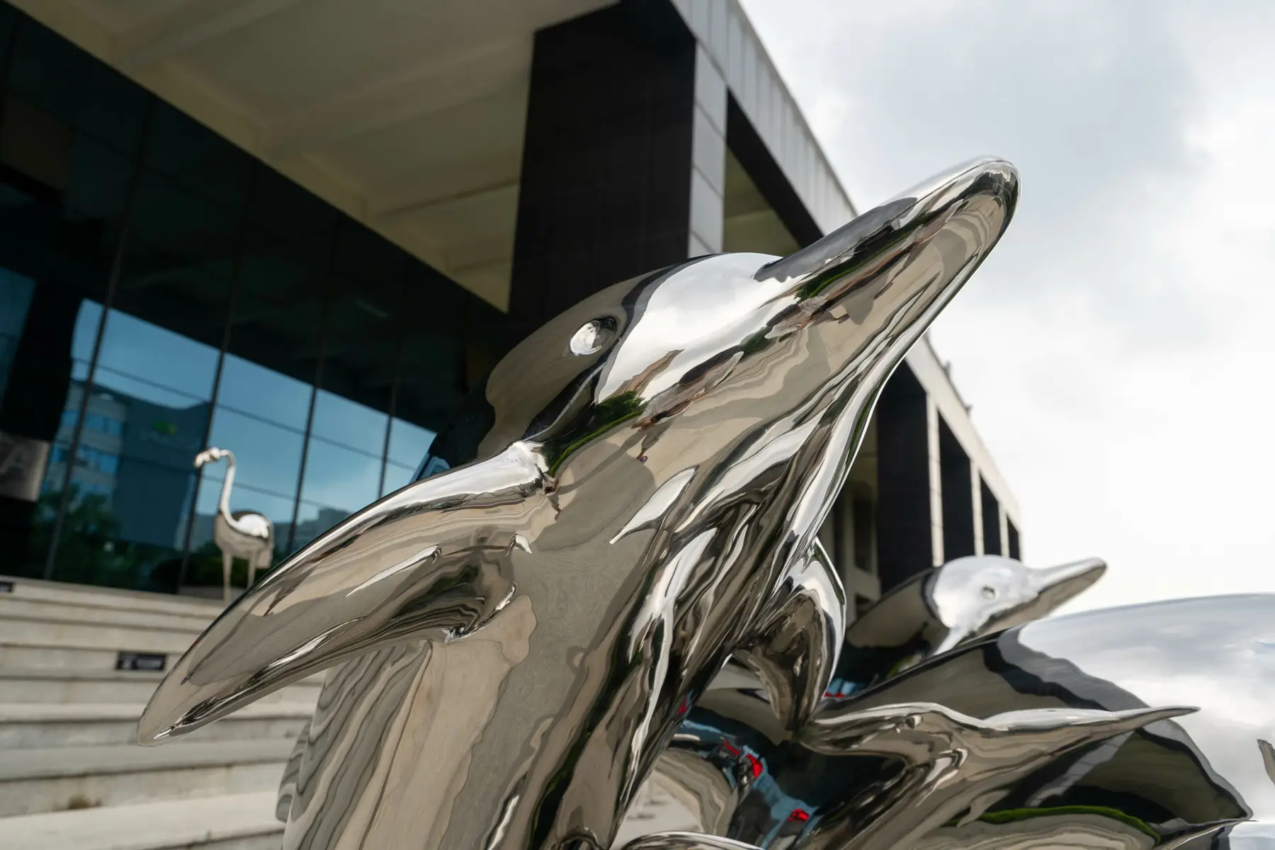 Two shiny metal dolphin sculptures outside a modern building.