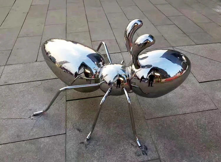 Giant stainless steel ant sculpture standing in a public park landscape
