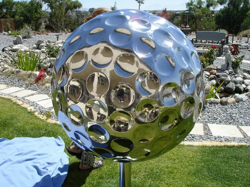 Hand forged stainless steel golf ball sculpture with mirror finish on a white wall