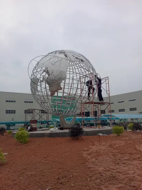 Stainless steel globe sculpture in a large urban plaza with people walking nearby